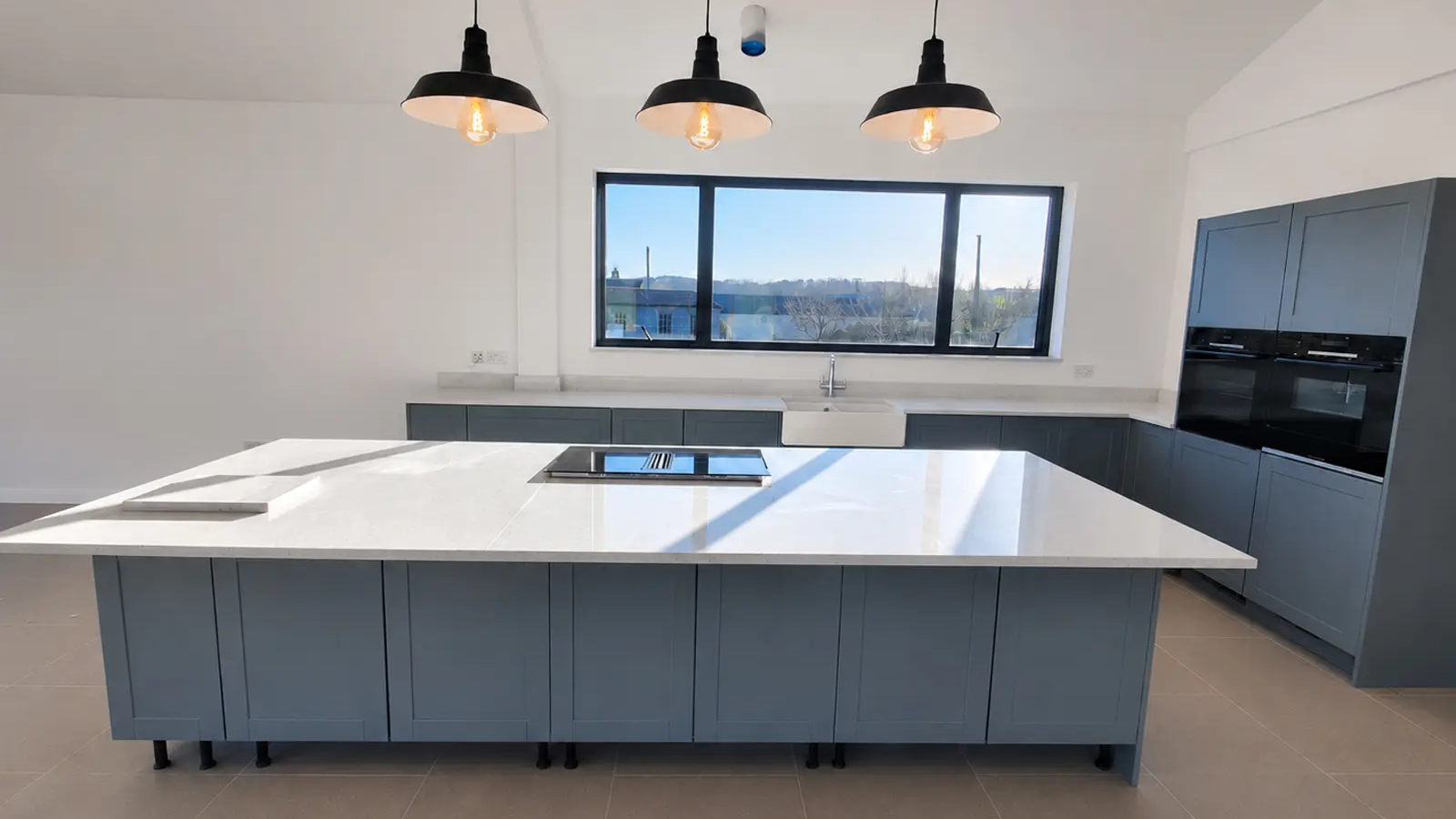 MonoLux customer kitchen with white quartz worktops, large island, hob cut-out and blue-grey cabinets.